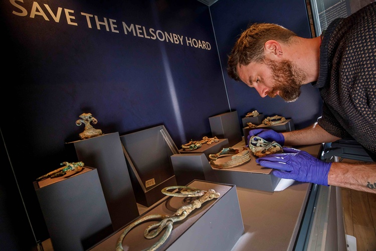 A person wearing gloves inspecting a metal artefact in a museum display