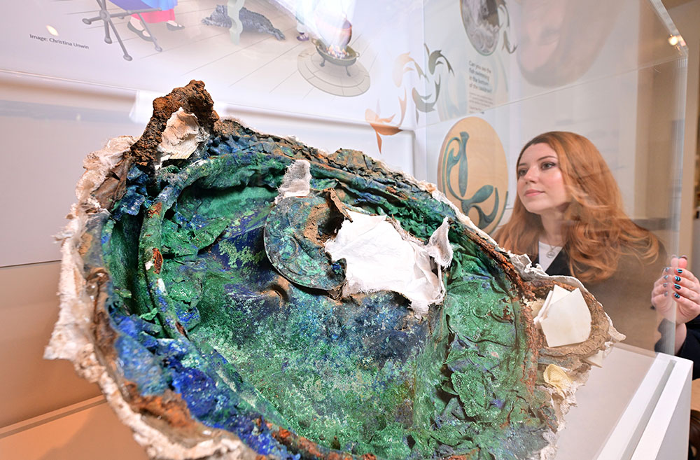 A woman looking into a museum cabinet containing a large piece of Iron Age metalwork.