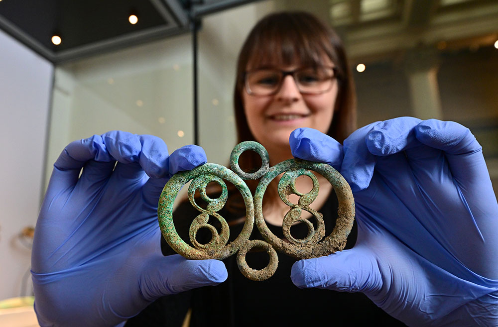 A woman wearing blue gloves holding a piece of decorative Iron Age metalwork
