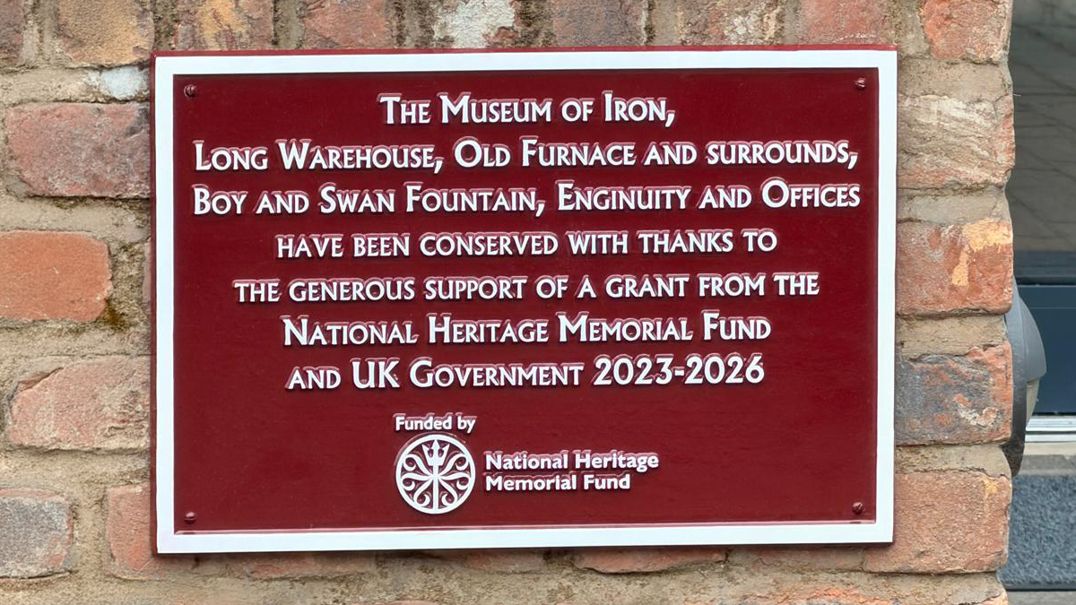 A maroon plaque shown at Ironbridge Gorge showing funding acknowledgement 