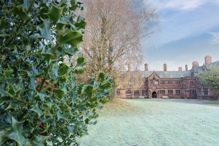 Gladstone's library seen from across the lawn with holly in the foreground and views of trees in front of the brick building with multiple chimneys