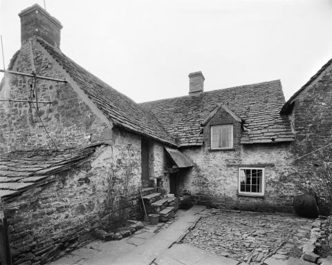 Medieval stone built house with two chimney, a door with steps leading up and small windows. Archive image in black and white.