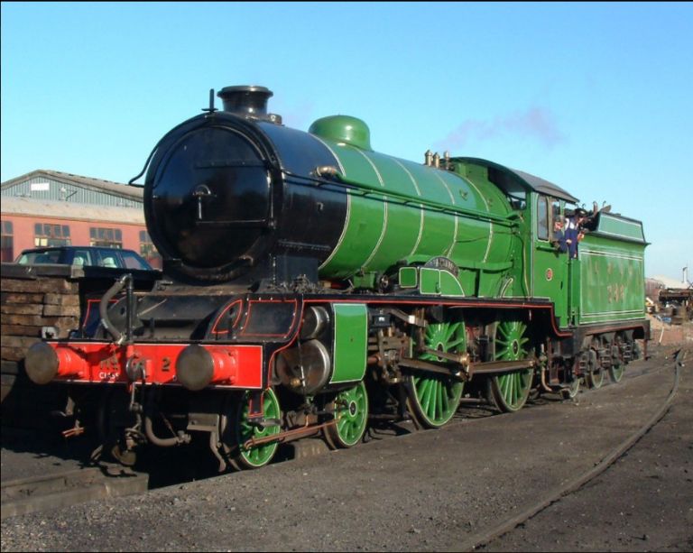 Close up view of Morayshire. A polished green steam locomotive with a black smokebox and red front stands on railway tracks in bright sunshine,