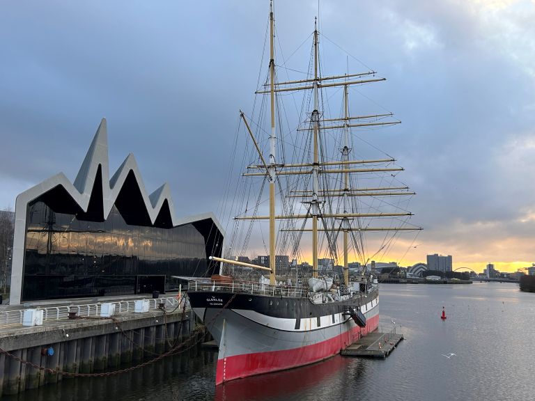 Tall Ship Glenlee seen on the River Clyde in Glasgow next to the Riverside Museum. It is a steel-hulled three-masted barque seen against a cloudy sky. 