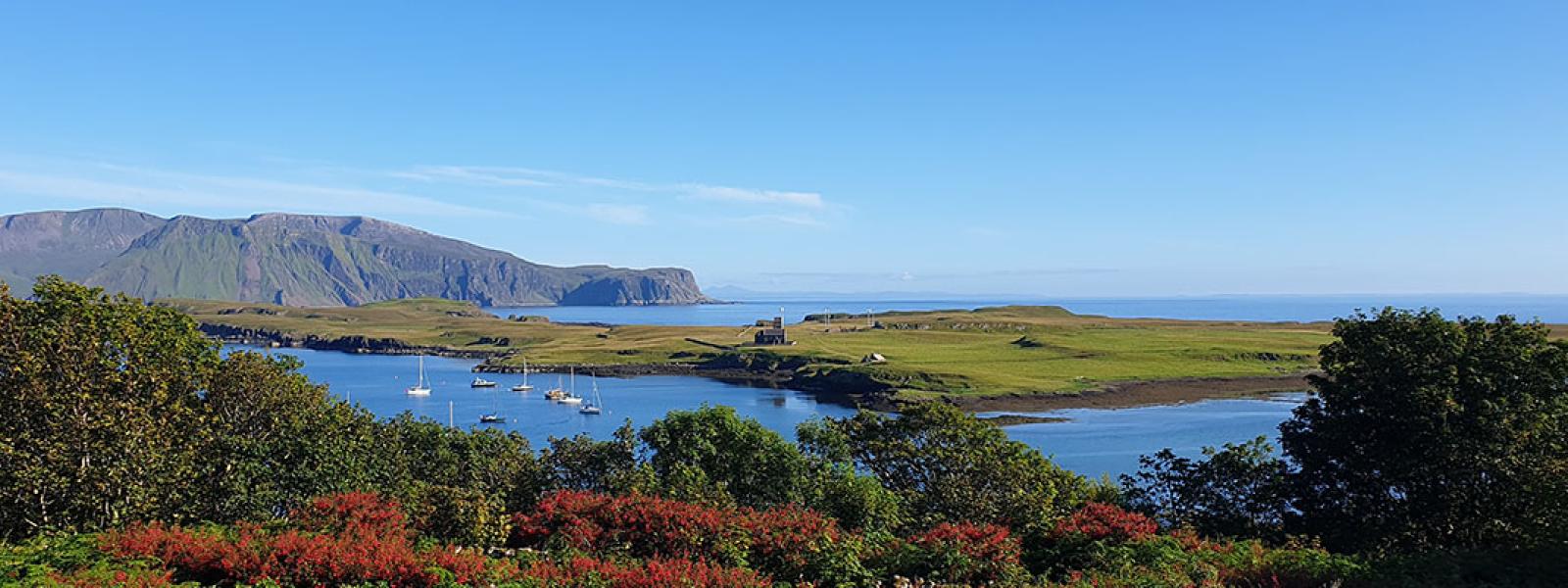 A view of the The Isle of Canna, with trees in the foreground, and mountains and lakes in the background