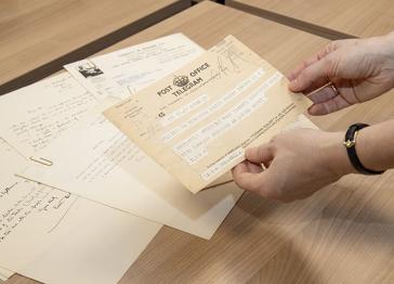 A close up of a person holding a telegram over a pile of archive documents