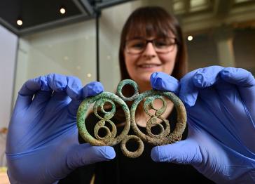 A woman wearing blue gloves holding a piece of decorative Iron Age metalwork