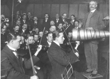 Black and white image featuring the composer Edward Elgar with an orchestra recording for a gramophone in the early twentieth century
