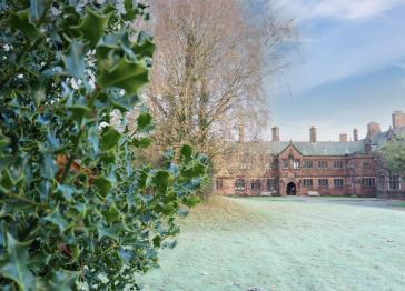 Gladstone's library seen from across the lawn with holly in the foreground and views of trees in front of the brick building with multiple chimneys