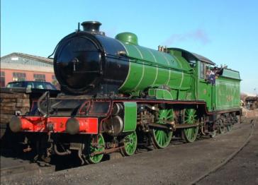 Close up view of Morayshire. A polished green steam locomotive with a black smokebox and red front stands on railway tracks in bright sunshine,