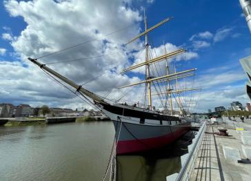 Tall Ship Glenlee seen on the River Clyde in Glasgow. It is a steel-hulled three-masted barque seen against a blue but cloudy sky. 