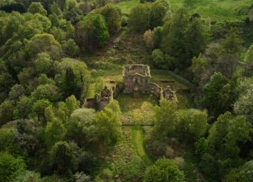 Mavisbank House aerial view showing the house in state of disrepair and surrounded by trees and greenery. 