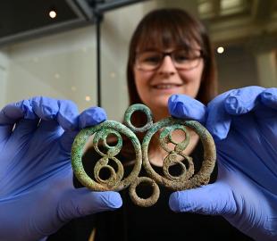 A woman wearing blue gloves holding a piece of decorative Iron Age metalwork